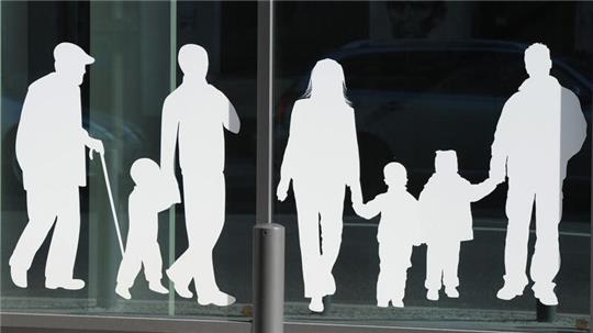 Silhouetten von Menschen in verschiedenem Alter sind auf Fensterscheiben aufgeklebt.