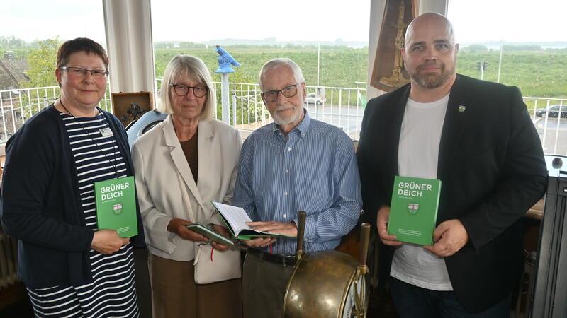Silke Ebers, Angelika Wirbals, Gerd Rieper und Bürgermeister Nikolai Müller halten das Buch „Grüner Deich" von Heinz Julius Rieper (1923-1991) auf der Kapitänsbrücke der Maritimen Landschaft in ihren Händen.