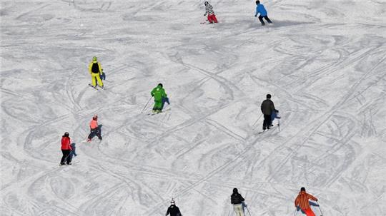 Skifahrer fahren bei Sonnenschein auf einer Skipiste.