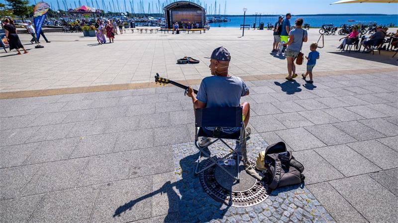 Sonniges Sommerwetter: Straßenmusiker spielt an der Promenade am Salzhaff