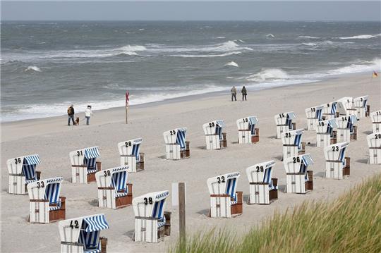 Spaziergänger gehen bei stürmischem Wetter am Weststrand von List entlang. Rund 40 Strandkörbe, die bisher am Strand von List standen, werden an diesem Samstag versteigert. Foto: picture alliance / dpa