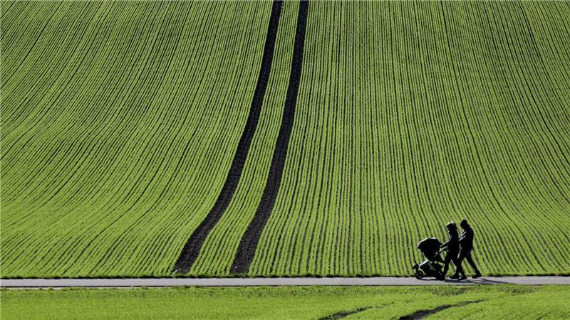 Spaziergänger gehen im Sonnenschein an einem frisch bestellten Feld in Baden-Württemberg vorbei.
