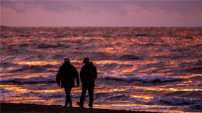 Spaziergänger sind nach Sonnenuntergang am Strand von Warnemünde an der Ostsee unterwegs.