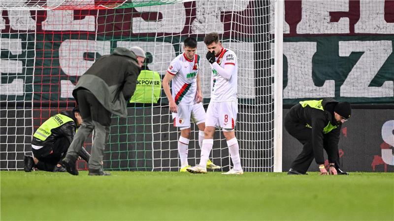 Spieler und Ordner sammeln nach dem Fanprotest Gegenstände vom Rasen.