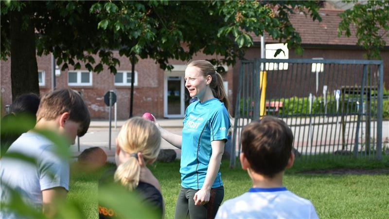 Sportlehrerin Marie-Luise Zentgraf steht vor ihrer Grundschulklasse, hält einen Wurfball in der rechten Hand und erklärt.