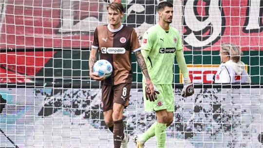 St. Paulis Eric Smith (l) und St. Paulis Torwart Nikola Vasilj (r) reagiert im Spiel. 