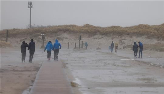 St. Peter-Ording: Strandbesucher kämpfen sich durch die Orkanböen. Foto: Axel Heimken/dpa