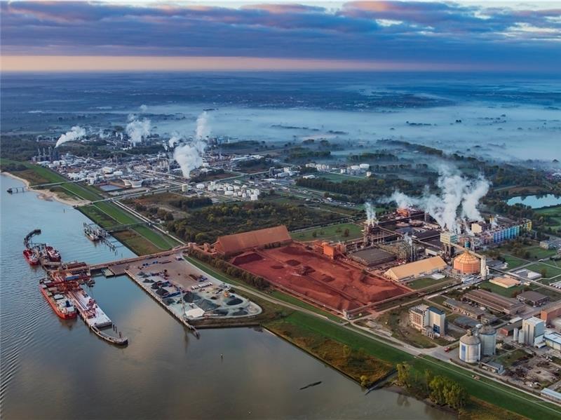 Stades Seehafen mit der Dow (links im Hintergrund) und der AOS. Gut zu sehen: Die Halden mit dem rot-braunen Bauxit, aus dem Aluminium gewonnen wird. Direkt rechts daneben das halb fertige Gebäude, wo eine Müllverbrennungsanlage geplant ist