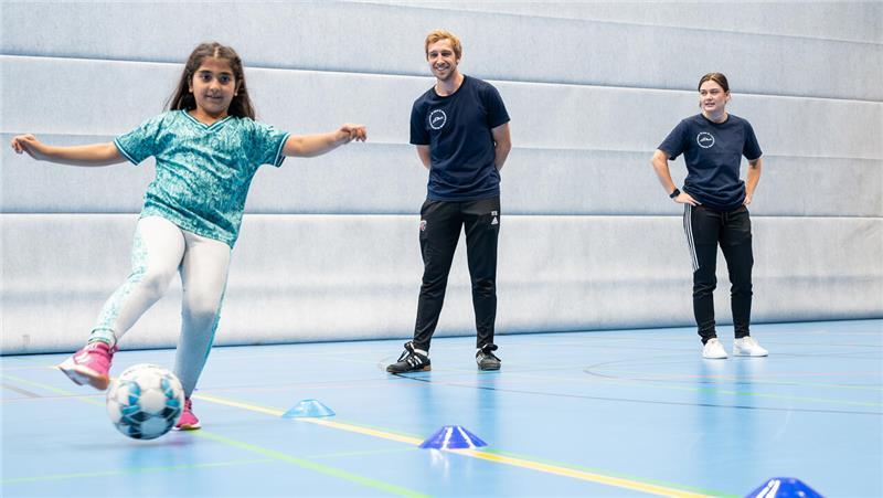 Stefan Schröder (M) und Friederike Kraft (r), beide Trainer bei „Sport vernetzt“ leiten zusammen eine Übungseinheit beim Fußball. Nicht alle Kinder haben Zugang zu Freizeitsport.
