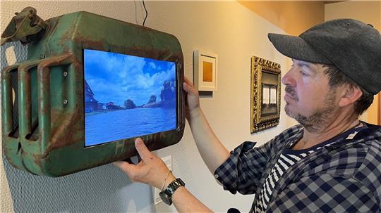 Steffen Gill hängt seinen an der Este gefundenen Tankkanister in der Ausstellung „Wassergeschichten im Dialog“ des Künstlerkollektivs Flunst in Estebrügge auf. Auf dem Bildschirm: eine Flussfahrt von Buxtehude bis Neuenfelde.