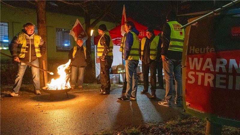 Streikende in Warnwesten wärmen sich in Augsburg an einem Feuer während eines Warnstreiks im ÖPNV.