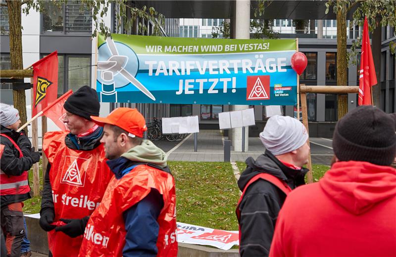 Streikende stehen mit einem Transparent mit der Aufschrift „Wir machen Wind bei Vestas! Tarifverträge Jetzt!“ auf dem Kapstadtring in der City Nord. Die IG Metall rief Beschäftigte aus dem gesamten Bundesgebiet zur Kundgebung vor der Deutschlandzentrale des Windanlagenherstellers Vestas in Hamburg auf. Foto: Georg Wendt/dpa