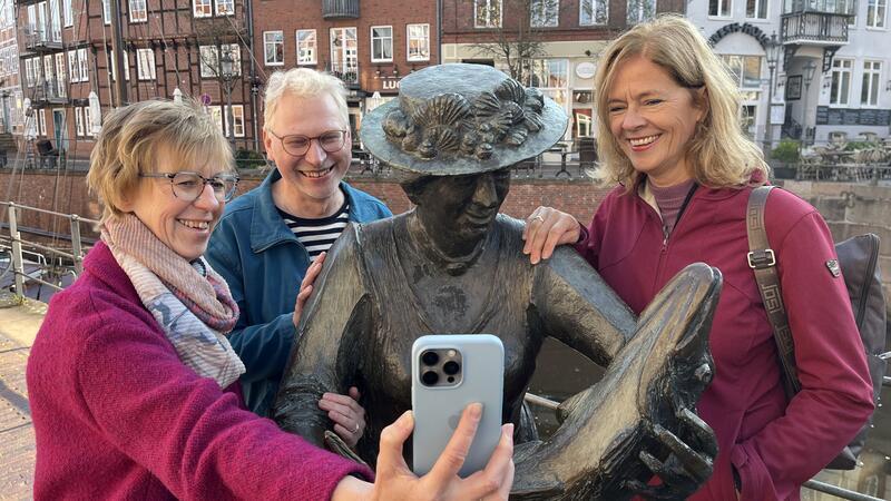 Mit Smartphone und Mutter Flint durch Stade und Steinkirchen Susanne Gratza, Frank Tinnemeyer und Ines Utecht zeigen Mutter Flint im historischen Hansehafen in Stade auf dem Smartphone, wie sie digital wieder zum Leben erweckt wurde (von links).