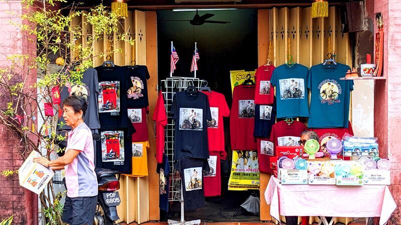 Penangs berühmte Street Art: „Malaysias Antwort auf Banksy“ T-Shirts und andere Dinge, auf denen Street Art-Kunstwerke aus Penang abgebildet sind, werden in einem Geschäft zum Kauf angeboten.