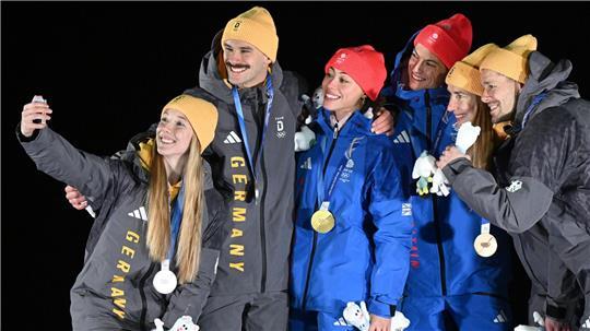 Tabitha Stoecker (Großbritannien) und Matt Weston (Großbritannien, beide M) posieren bei der Siegerehrung ihren Goldmedaillen nach dem Skeleton-Team-Wettbewerb neben Susanne Kreher (Deutschland, l) und Axel Jungk (Deutschland, 2.v.l.) mit der Silbermedaille und Jacqueline Pfeifer (Deutschland, 2.v.r.) und Christopher Grotheer (Deutschland) mit der Bronzemedaille bei den Olympischen Winterspielen Mailand Cortina 2026.