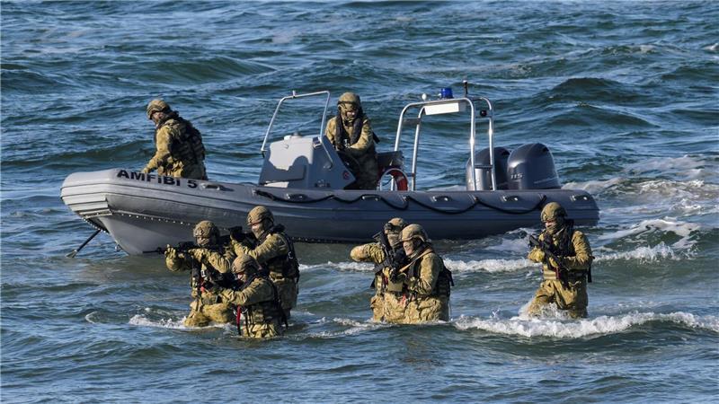 Taucher machen den Anfang und steigen aus dem Wasser auf den schneebedeckten Strand, um den Küstenabschnitt zu sichern.