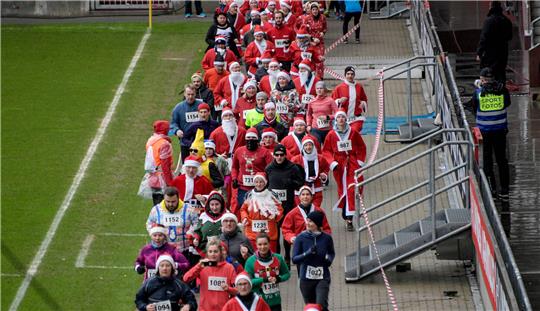 Teilnehmer des X-Mass Run St. Pauli laufen in weihnachtlichen Verkleidungen durch das Millerntorstadion. Foto: Axel Heimken/dpa