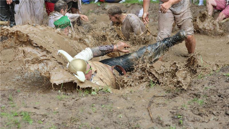 Teilnehmer springen auf dem Dreckschweinfest 2025 auf dem Festivalgelände auf der Wildbahn in ein Schlammloch. 