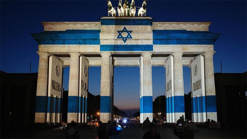 Teilnehmer stehen vor dem mit der Fahne Israels angestrahlten Brandenburger Tor und gedenken bei der Veranstaltung zum Jahrestag des Terrorangriffs der Hamas auf Israel am 7. Oktober 2023 den Opfern.