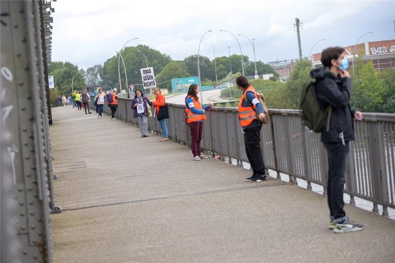 Teilnehmer und Teilnehmerinnen der Menschenkette stehen nahe der Hafencity auf einer Brücke über die Elbe. Foto: Jonas Walzberg/dpa