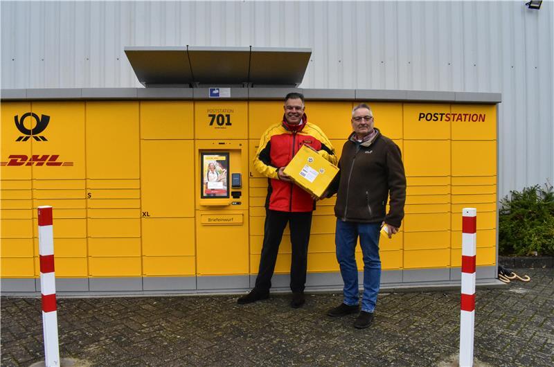 Thorn Schütt von der Deutschen Post und Dollerns Bürgermeister Jan-Hinnerk Burfeind weihen die neue Poststation mit einem ersten Testpaket ein.
