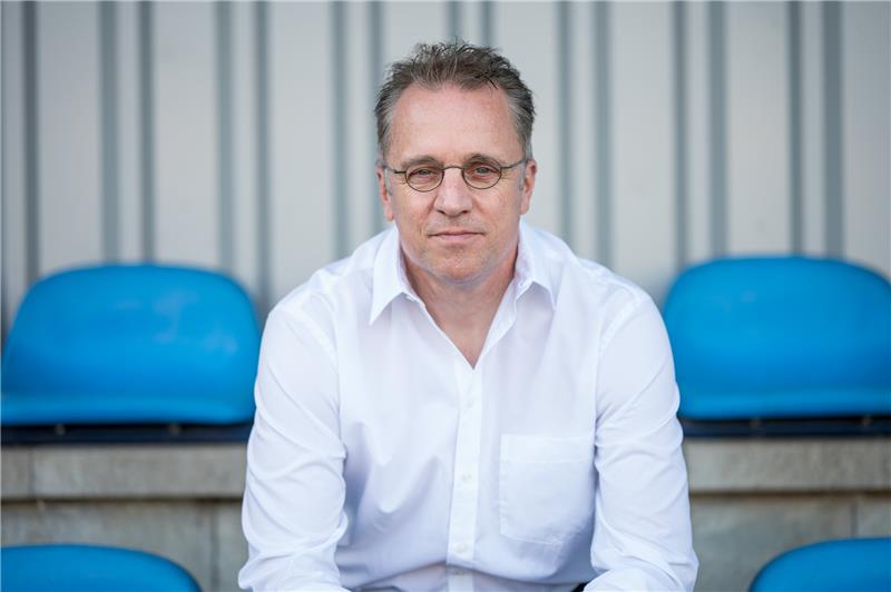 Tim Meyer, DFB-Chefmediziner, sitzt auf überdachten Sitzplätzen auf einem Fußballplatz. Foto: Oliver Dietze/dpa