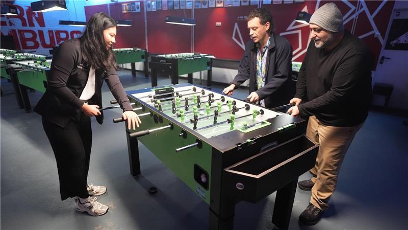 Tischkicker-Weltmeisterin Linh Tran zeigt ihr Können den beiden Schauspielern.