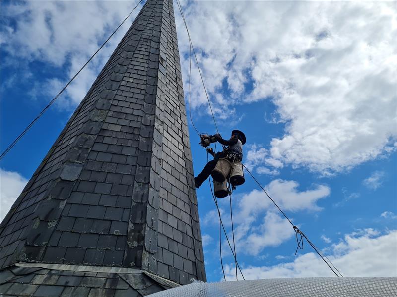 Arbeiten in schwindelerregender Höhe: Kletternde Dachdecker in Assel Torben Hasenberg lässt sich in über 20 Metern Höhe den Kirchturm der St.-Martin-Kirche hinaufziehen. Den Aufstieg erleichtert ihm das Seilmoped in seiner linken Hand. Foto: Stahmann