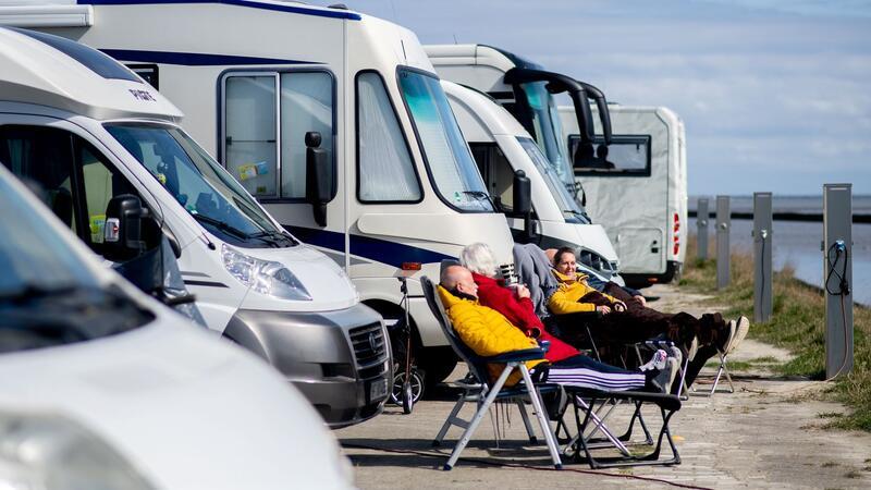 Touristen aus Nordrhein-Westfalen sitzen bei sonnigem Wetter vor ihren Wohnmobilen und blicken auf das Wattenmeer.