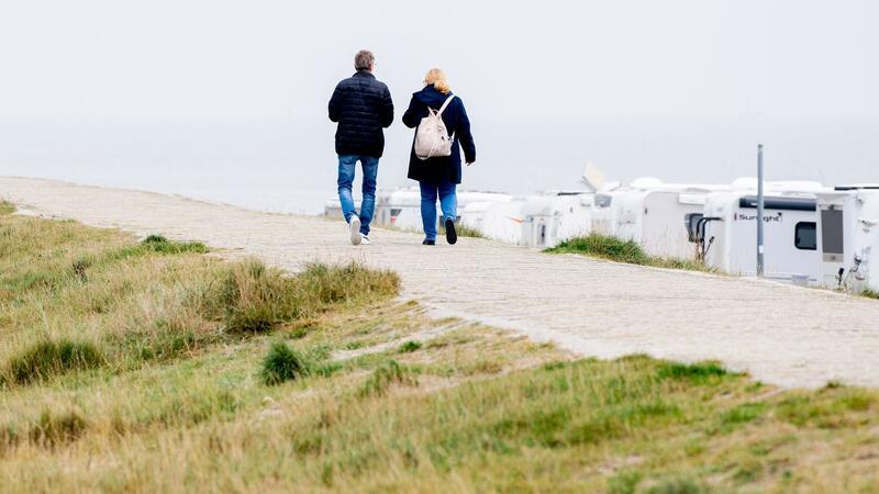 Urlaubsregionen mit Buchungen vor Herbstferien zufrieden Touristen gehen bei trübem Wetter auf einem Deich vor der Nordsee entlang.