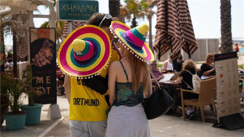 Touristen mit bunten Hüten stehen beim Start der Ballermann-Saison auf Mallorca an einer Bar.