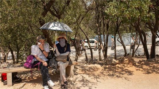 Touristen unter Bäumen am Eingang der Akropolis im Hitzesommer 2023.