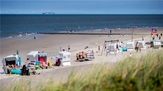 Touristinnen und Tourstien sitzen bei sonnigem Wetter in Strandkörben am Strand der Insel Wangerooge.