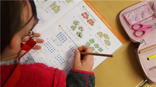 Typisch Grundschule: Eine Schülerin schreibt im Unterricht in ihr Schulbuch und löst eine Rechenaufgabe.