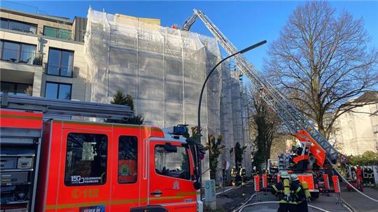 Über eine Drehleiter löschen Feuerwehrleute Glutnester auf dem Dach einer Baustelle ab.