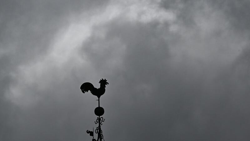 Über einem Wetterhahn schweben dunkle Regenwolken.