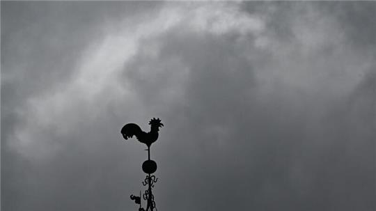 Über einem Wetterhahn schweben dunkle Regenwolken.