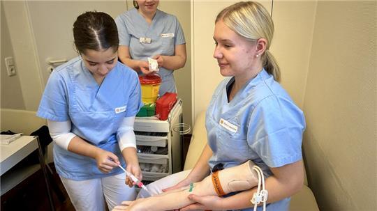 Übung beim Azubi-Infotag: Lara Kaouach, Lilli Krause und Emily Wist nehmen Blut am Trainingsarm ab.