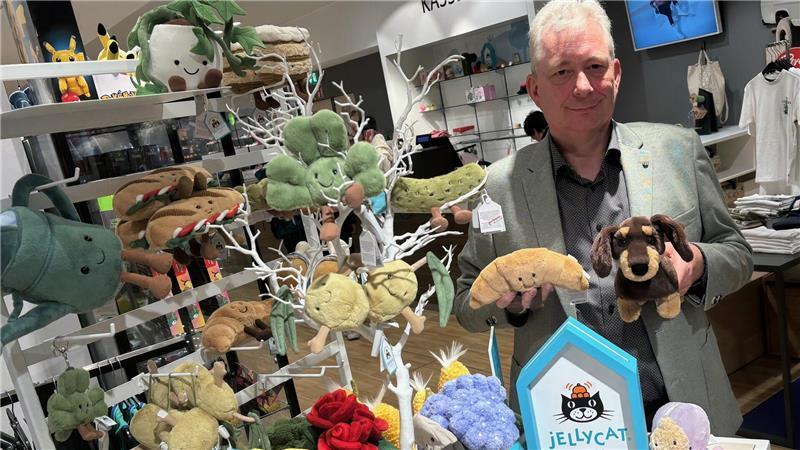 Um die Plüschtiere von Jellycat ist ein Hype im Internet entstanden. Dietmar Höft, Leiter der Spielewelt bei Stackmann, hält zwei der Trendartikel in den Händen: ein Croissant und einen Dackel.