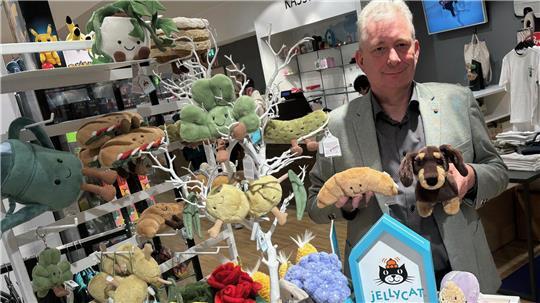 Um die Plüschtiere von Jellycat ist ein Hype im Internet entstanden. Dietmar Höft, Leiter der Spielewelt bei Stackmann, hält zwei der Trendartikel in den Händen: ein Croissant und einen Dackel.