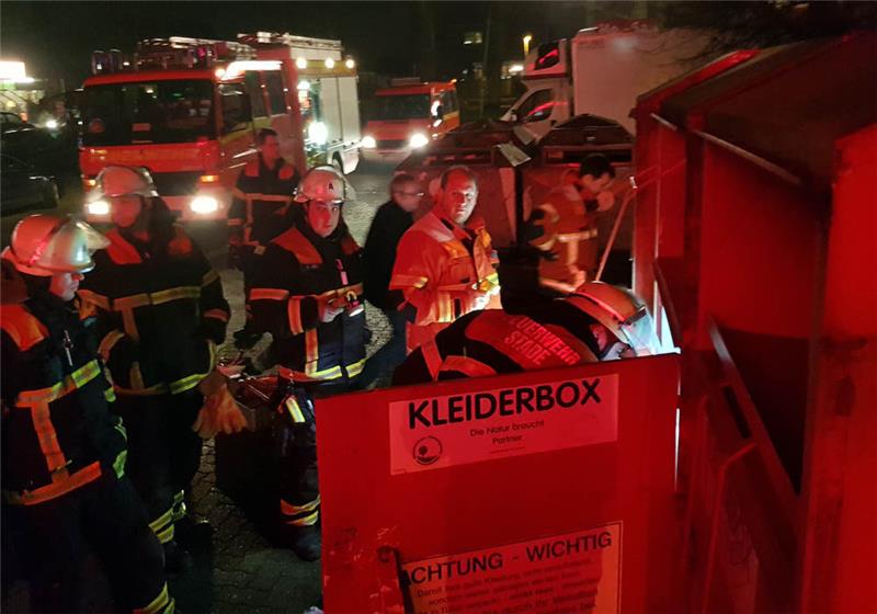 Umringt von Schaulustigen suchen die Rettungskräfte eine Katze in den Altkleider-Boxen. Fotos: Beneke