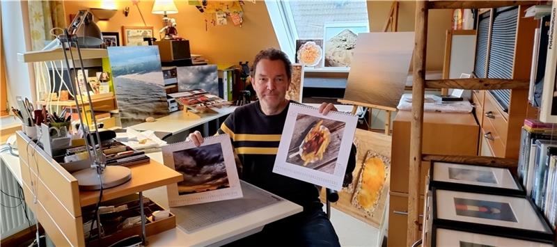 Umringt von quadratischen Fotos in allen Größen in seinem Arbeitszimmer unterm Dach: Der Bliedersdorfer Hobbyfotograf und Grafik-Designer Volker Groneberg zeigt seine beiden Jahreskalender 2023. Foto: Lohmann