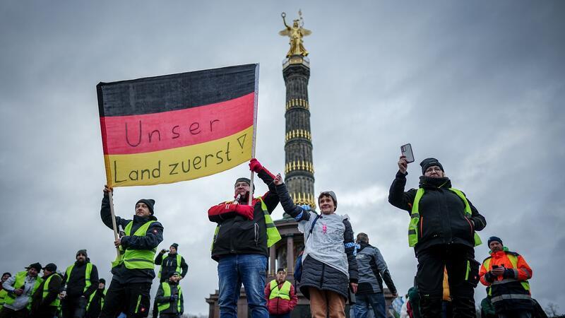 Bauernprotest ohne schnelle Diesel-Lösung „Unser Land zuerst!“ - Teilnehmer der Großkundgebung protestieren mit einer Deutschlandfahne vor der Siegerssäule.