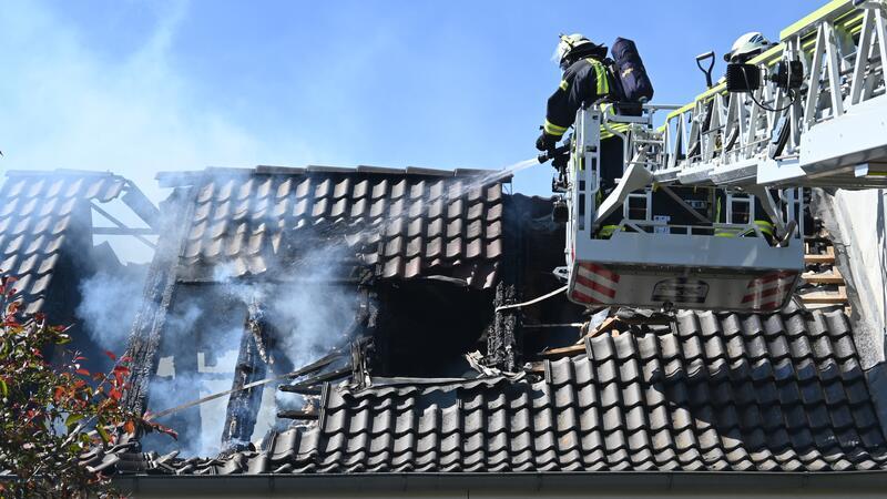Unter Atemschutz bekämpfen Feuerwehrleute im Juni 2023 den Brand im Dachstuhl in Steinkirchen mit Hilfe der Drehleiter aus Harsefeld. Im Inneren sind Löschtrupps im Einsatz, gemeinsam werden auf dem Dach des Hinterhauses die Pfannen entfernt.