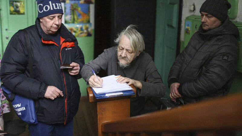 Bilder des Tages Unter Aufsicht: Ein Mann füllt in der sibirischen Stadt Omsk seinen Stimmzettel für die Präsidentenwahl in Gegenwart eines mobilen Wahlkomitees aus, das all diejenigen besucht, die nicht in der Lage sind, zu den Wahllokalen zu gehen.