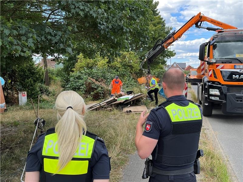 Unter Polizeischutz räumen Mitarbeiter der Straßenmeisterei und des Kreis-Umweltamtes den Müll und Stacheldraht an der K 34 weg. Foto Vasel