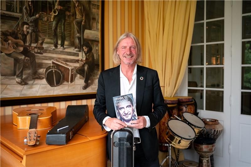 Unternehmer Frank Otto steht mit seinem neuen Buch in einem Zimmer voller Musikinstrumente. Foto: Walzberg/dpa