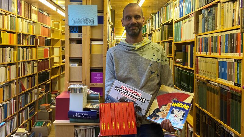 Hans-Uwe Hansen: Alle dürfen noch mal in seiner Privatbibliothek stöbern Tobias Rothenberg steht mit einer Buchauswahl in den Händen zwischen den gefüllten Regalen von Hans-Uwe Hansens ehemaliger Privatbibliothek