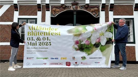 Veranstaltungsmanagerin Miriam Stöckmann und Bürgermeister Matthias Riel halten einen Werbebanner für das Altländer Blütenfest am 3./.4. Mai in ihren Händen.