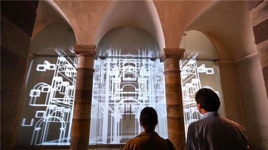 Vertreter des Presseteams stehen nach der Pressekonferenz vor der Medienwand im Unesco-Welterbe Corvey auf der eine 3D-Animation des Westwerks zu sehen ist.